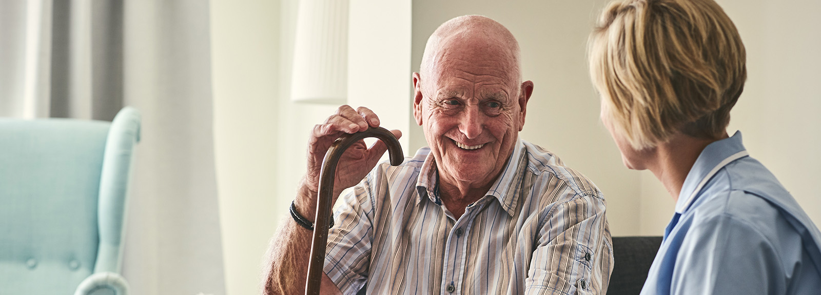 Smiling retired senior man sitting on sofa with female home carer at care home